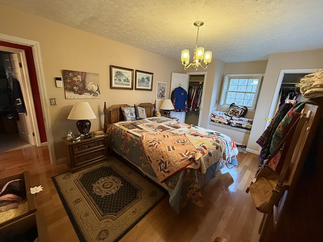 bedroom with a notable chandelier, a textured ceiling, baseboards, and wood finished floors