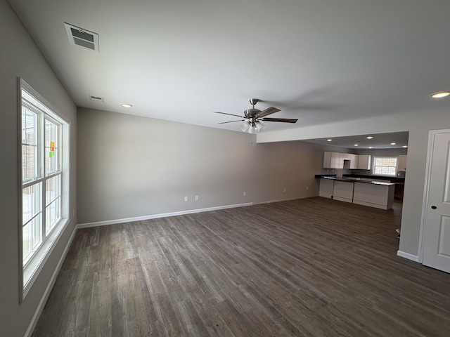 unfurnished living room featuring dark wood-type flooring, a healthy amount of sunlight, and visible vents