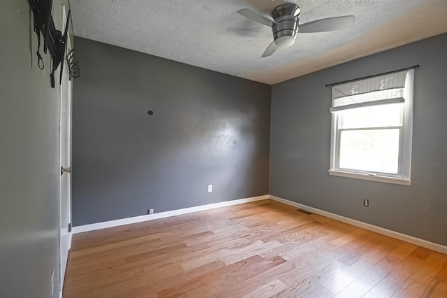 empty room featuring a textured ceiling, visible vents, a ceiling fan, baseboards, and light wood finished floors