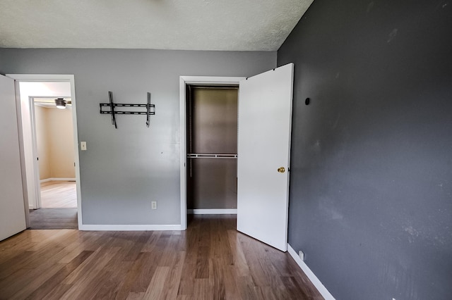 unfurnished bedroom featuring a closet, a textured ceiling, baseboards, and wood finished floors