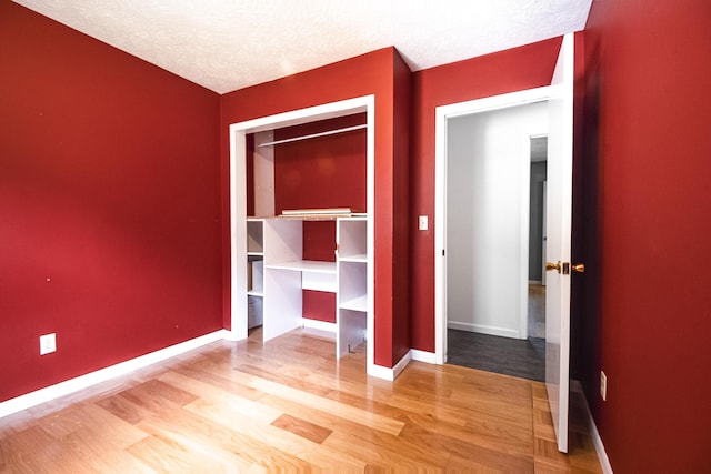 unfurnished bedroom with a textured ceiling, baseboards, and wood finished floors