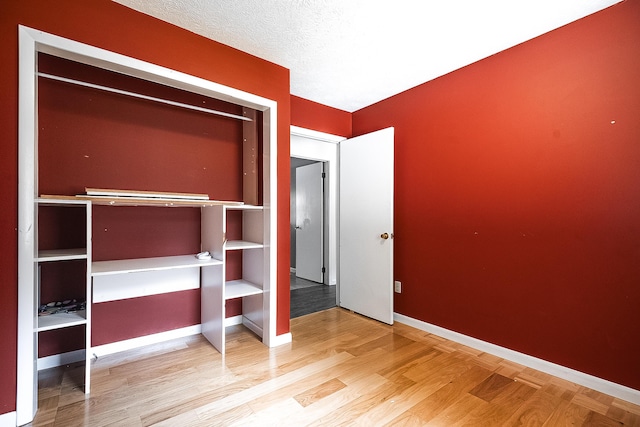 unfurnished bedroom featuring a closet, a textured ceiling, baseboards, and wood finished floors