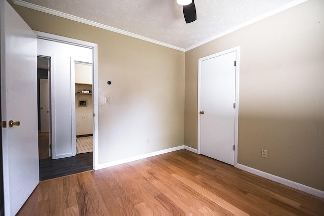 unfurnished room with ornamental molding, a textured ceiling, baseboards, and wood finished floors