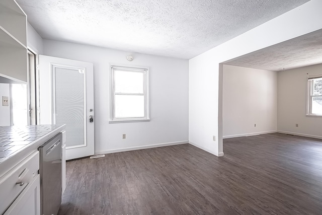 unfurnished dining area with a textured ceiling, baseboards, and dark wood-type flooring