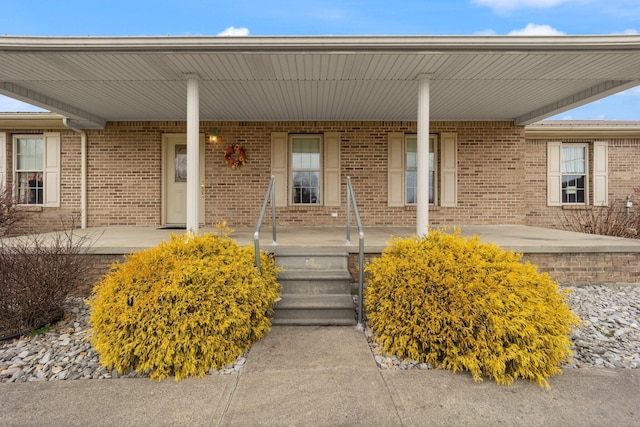 doorway to property featuring a porch and brick siding