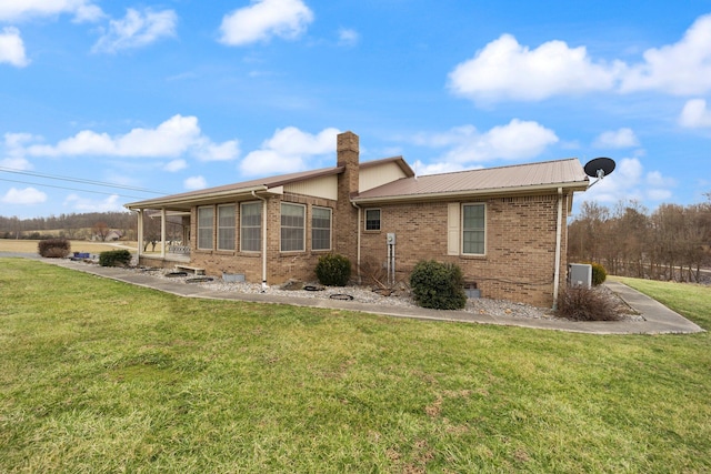 rear view of property featuring metal roof, a chimney, crawl space, brick siding, and a lawn