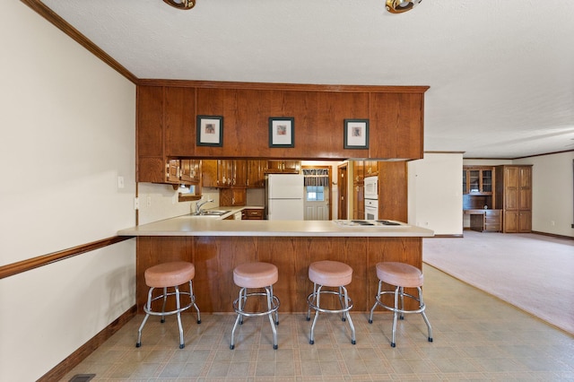 kitchen with a sink, light carpet, a peninsula, baseboards, and white appliances