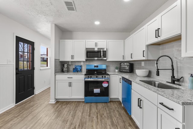 kitchen featuring light wood-style flooring, a sink, visible vents, white cabinetry, and appliances with stainless steel finishes