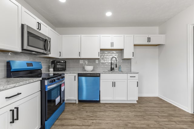 kitchen with wood finished floors, light stone countertops, stainless steel appliances, white cabinetry, and a sink