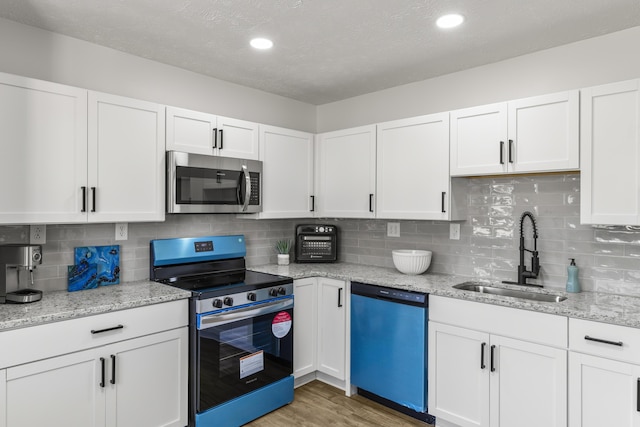 kitchen with light stone counters, light wood-style flooring, stainless steel appliances, a sink, and white cabinetry