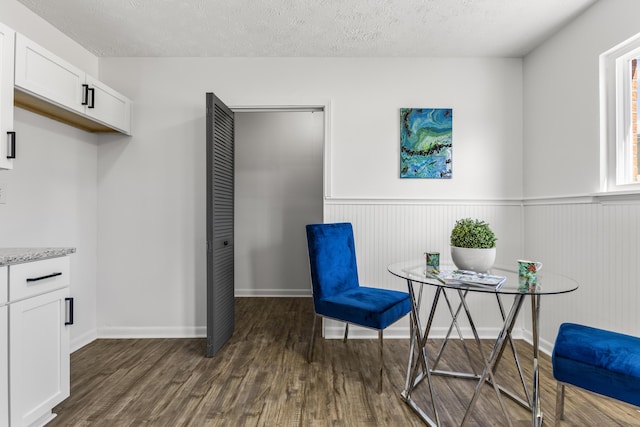 living area featuring a wainscoted wall, a textured ceiling, baseboards, and dark wood-type flooring