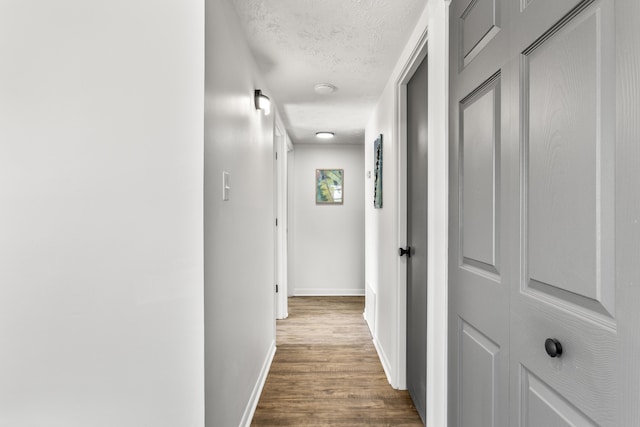 corridor featuring baseboards, a textured ceiling, and wood finished floors