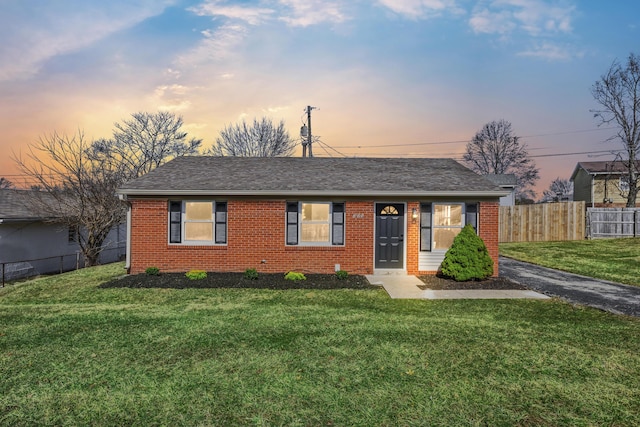 single story home featuring brick siding, roof with shingles, a front yard, and fence