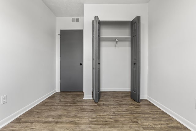 unfurnished bedroom with baseboards, visible vents, wood finished floors, a textured ceiling, and a closet