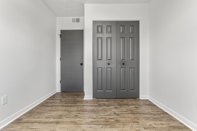 unfurnished bedroom featuring a closet, wood finished floors, visible vents, and baseboards