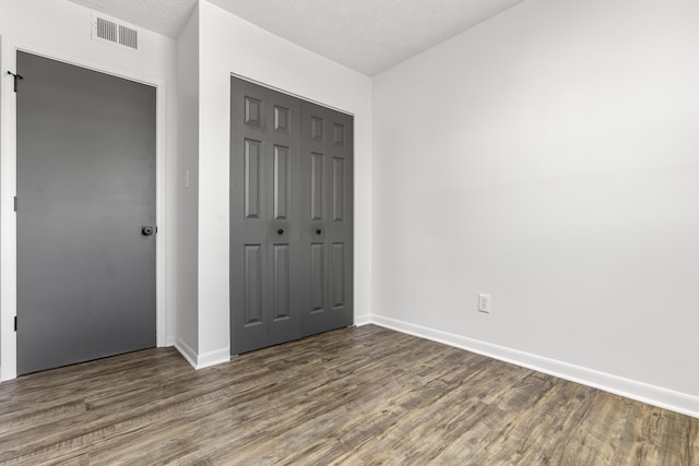 unfurnished bedroom with a textured ceiling, a closet, visible vents, and wood finished floors