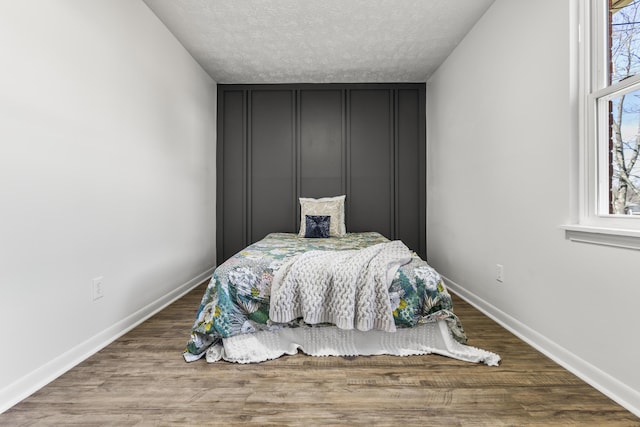 bedroom featuring a textured ceiling, baseboards, and wood finished floors