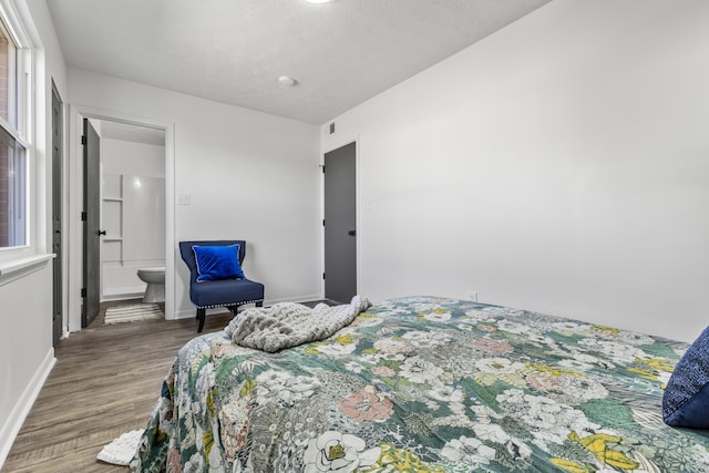 bedroom with visible vents, connected bathroom, baseboards, and wood finished floors