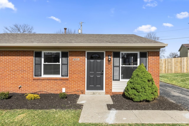 bungalow-style home featuring roof with shingles, fence, and brick siding