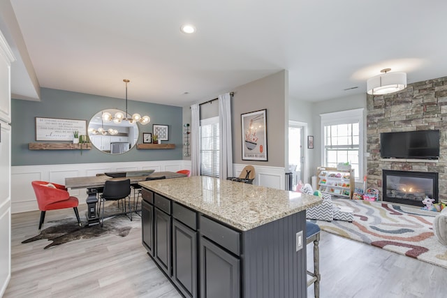 kitchen with a wainscoted wall, open floor plan, a center island, a fireplace, and pendant lighting