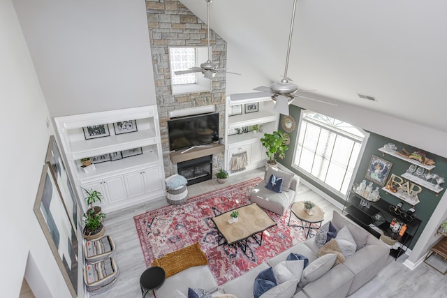 living room with a fireplace, visible vents, light wood-style flooring, ceiling fan, and high vaulted ceiling