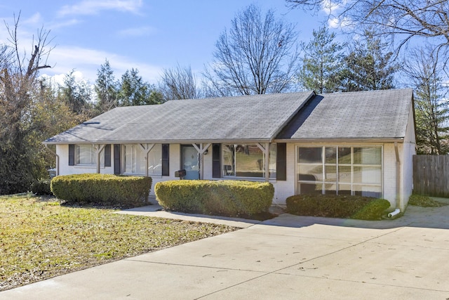 single story home featuring brick siding, a shingled roof, fence, and a front yard