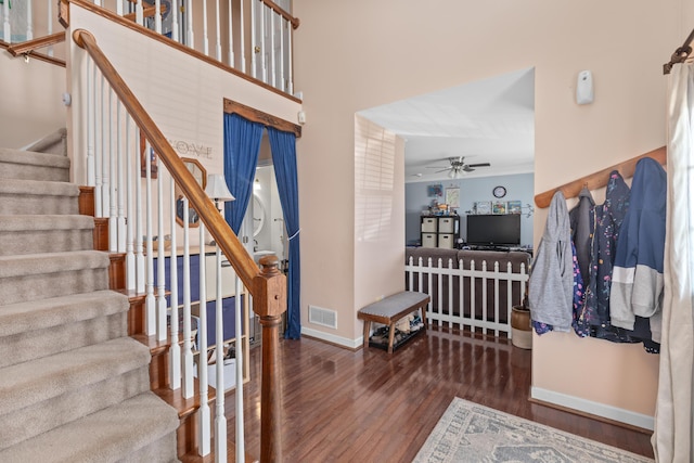 stairway with baseboards, visible vents, a ceiling fan, wood finished floors, and a high ceiling