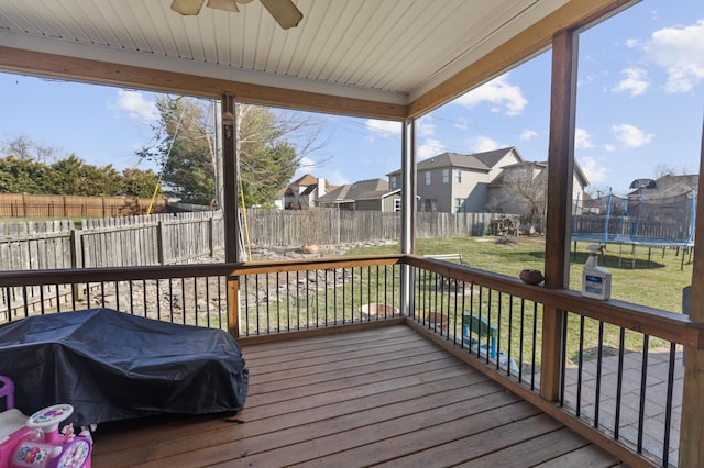 wooden terrace with area for grilling, a ceiling fan, a lawn, a residential view, and a trampoline