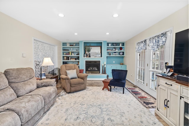 living room featuring built in shelves, recessed lighting, and a fireplace with raised hearth