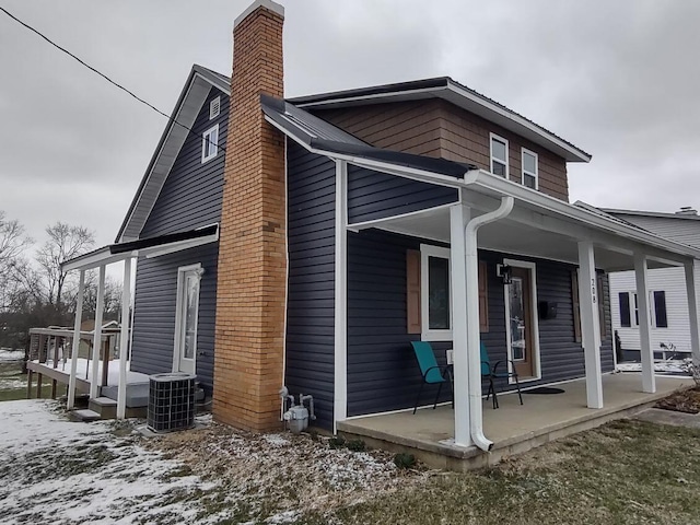 rear view of property with central air condition unit, covered porch, and a chimney