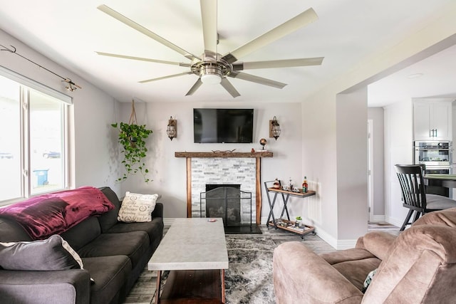 living area featuring a ceiling fan, a fireplace, and baseboards