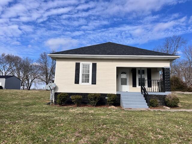 bungalow-style home featuring covered porch, a front lawn, and roof with shingles