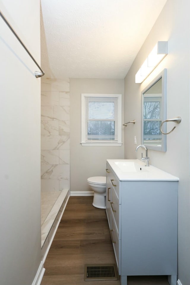 full bath featuring toilet, a shower stall, vanity, wood finished floors, and baseboards