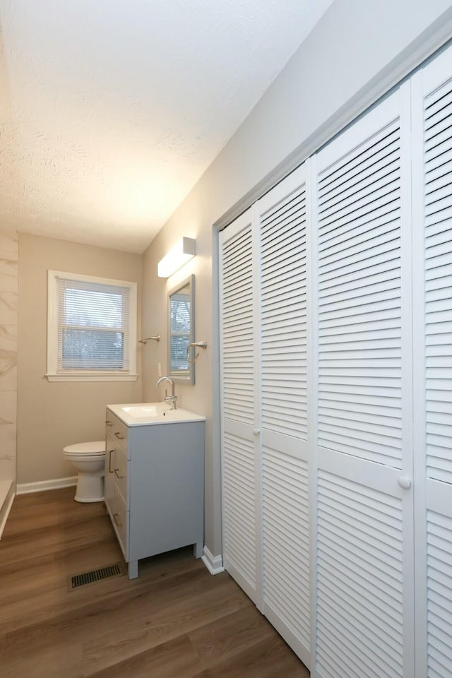 bathroom with a closet, visible vents, toilet, vanity, and wood finished floors