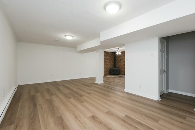 finished below grade area with a wood stove, a baseboard radiator, baseboards, and wood finished floors