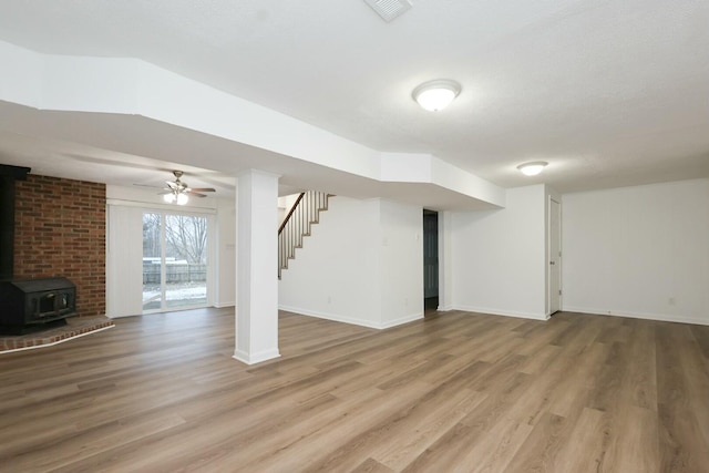 basement featuring visible vents, stairway, a wood stove, wood finished floors, and baseboards