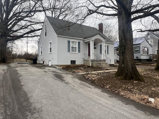 view of front of property featuring aphalt driveway, roof with shingles, and a chimney