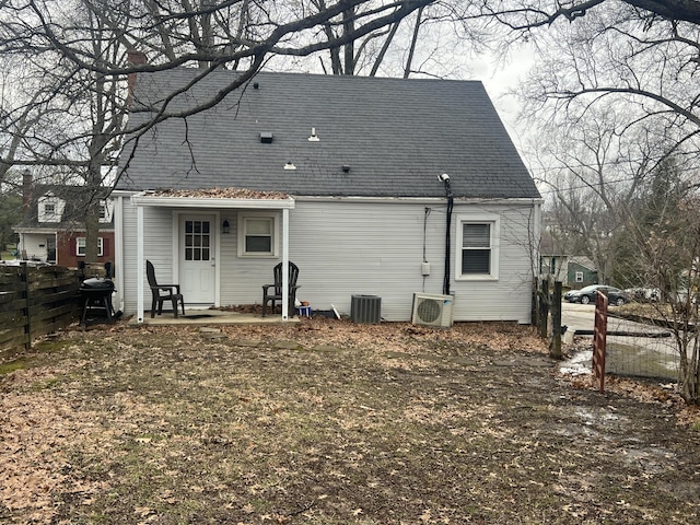 rear view of property with ac unit, roof with shingles, fence, and central AC