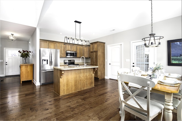 kitchen featuring hanging light fixtures, brown cabinetry, stainless steel appliances, and dark wood finished floors