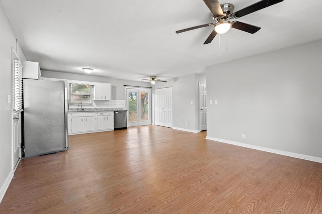 unfurnished living room featuring light wood finished floors, a sink, a ceiling fan, and baseboards