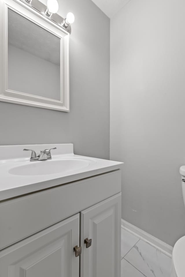 bathroom with toilet, marble finish floor, baseboards, and vanity