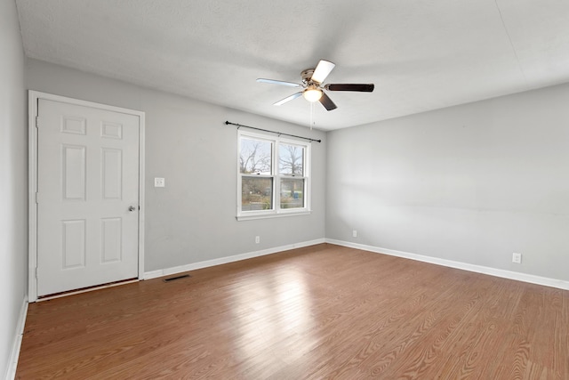 unfurnished room with a ceiling fan, visible vents, baseboards, and wood finished floors