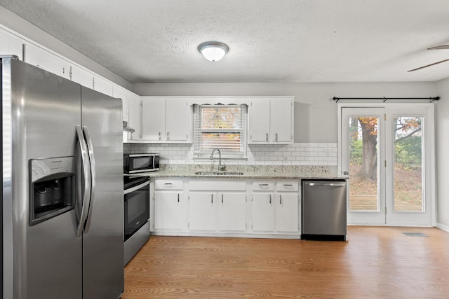 kitchen with stainless steel appliances, a sink, white cabinetry, and light wood-style floors