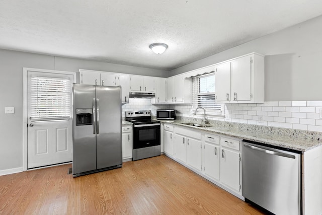 kitchen with stainless steel appliances, white cabinets, a sink, and under cabinet range hood