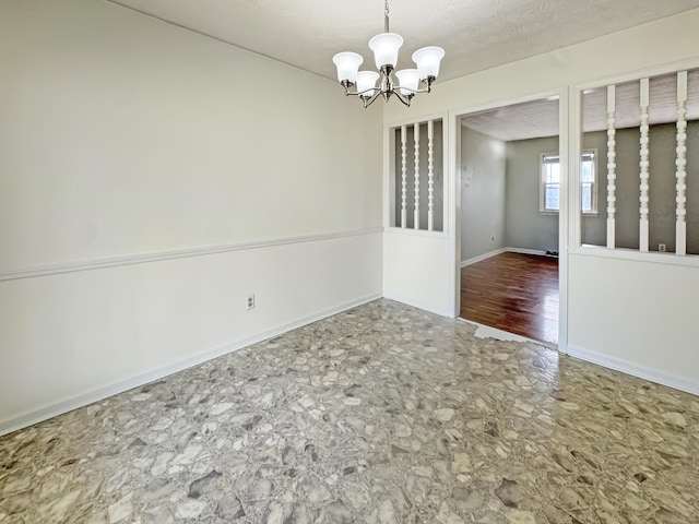 spare room featuring a textured ceiling, baseboards, and a notable chandelier