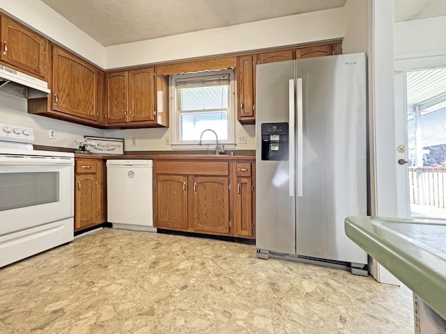 kitchen with white appliances, brown cabinets, a sink, and under cabinet range hood