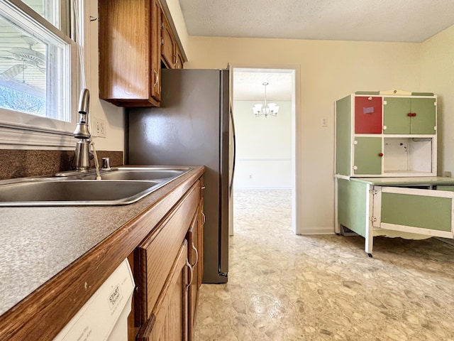 kitchen featuring a textured ceiling, white dishwasher, a sink, brown cabinets, and decorative light fixtures