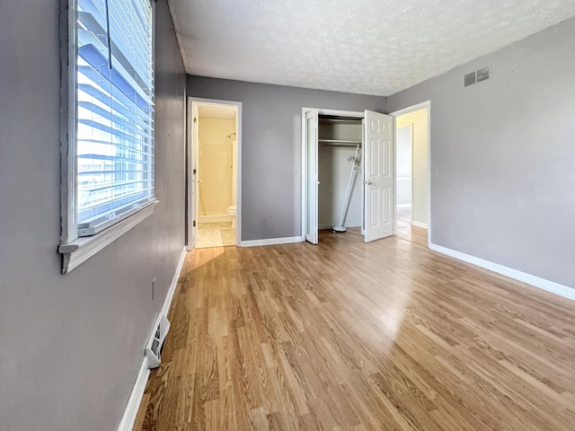 unfurnished bedroom with light wood-type flooring, visible vents, a textured ceiling, and baseboards