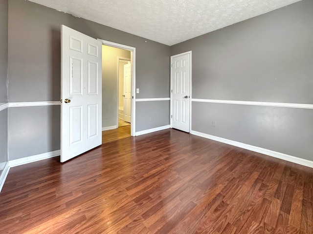 spare room featuring dark wood-style flooring, a textured ceiling, and baseboards