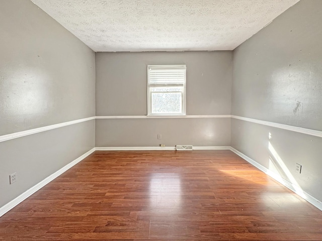 spare room featuring visible vents, a textured ceiling, baseboards, and wood finished floors